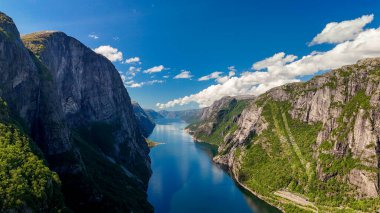 Sakin bir fiyordun yanında nefes kesici uçurumlar yükselir, Norveç 'teki canlı mavi gökyüzünü ve taze yeşilliği yansıtır. Lysefjord Lysebotn Norveç