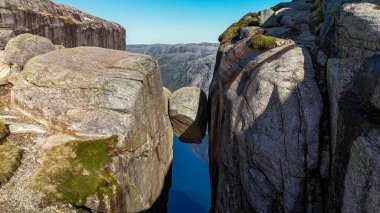 Norveç 'in dramatik uçurumlarına ve canlı gökyüzüne karşı durgun suların üzerinde dengede duran kayanın çarpıcı bir görüntüsü. Kjerag Kjeragbolten Lysefjord Norveç