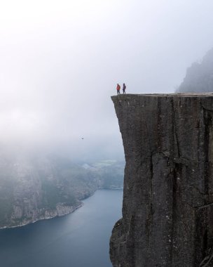 İki yürüyüşçü engebeli bir uçurumun kenarından alttaki fiyordun etrafını saran sisle nefes kesici manzaraya hayret eder. Önceki Norveç