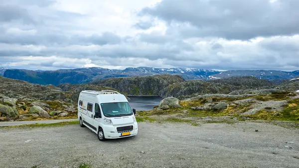 stock image A camper van rests on rocky ground overlooking Norway's breathtaking fjords under a moody sky.