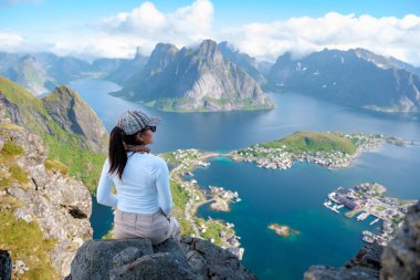 Bir gezgin, parlak mavi gökyüzünün altındaki gür dağlara ve dingin sulara hayran, nefes kesici Lofoten Adaları 'na bakıyor. Reinebringen Lofoten Norveç