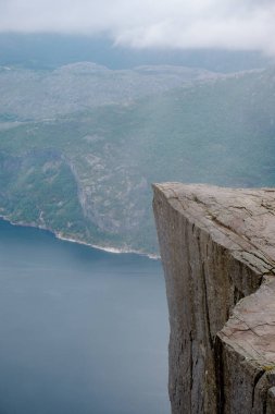 Engebeli bir uçurumun kenarından nefes kesici bir manzara yüksek dağlar ve sisle çevrili sakin bir fiyort ortaya çıkarır. Önceki Norveç