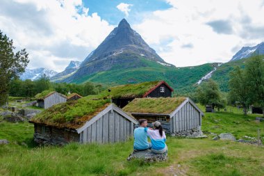 Bir çift aşık, bir kayanın üzerinde soluk kesici dağ manzarasına ve büyüleyici kulübelere hayran kalarak rahatlıyor. İç Norveç