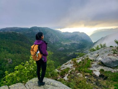 A solitary hiker stands on a rocky outcrop, absorbing the breathtaking views of Norway's lush valleys and distant mountains as dawn breaks. Preikestolen Norway clipart