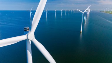 Uzun rüzgar türbinleri, Hollanda 'daki güneşli gökyüzünün zeminine karşı yenilenebilir enerjiyi kullanarak sakin sularda zarifçe dönüyor..