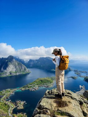 Yalnız bir yürüyüşçü engebeli bir uçurumun tepesinde duruyor, açık mavi gökyüzünün altında Norveç 'in Lofoten Adaları' nın nefes kesici manzaralarına dalmış..