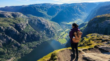 Yalnız bir yürüyüşçü nefes kesen bir uçurumun kenarında durup altın sabah ışığında yıkanan geniş fiyortlara ve yemyeşil manzaralara hayran kalır. Lysefjord Kjeragbolten Norveç