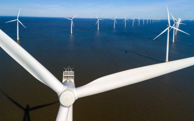 Parıldayan rüzgâr türbinleri engin denize karşı dimdik durur. Güneş batarken huzurlu bir Hollanda manzarasında enerjilerini kullanırlar. Hollanda 'da bir yel değirmeni parkında insansız hava aracı görüntüsü