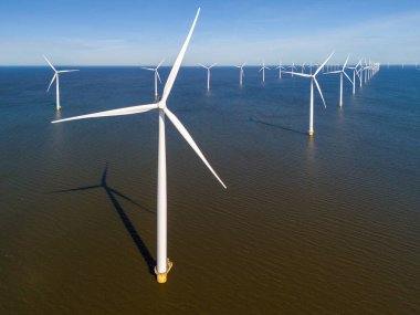 Işıl ışıl yanan yel değirmenleri durgun suların üzerinde dimdik durur. Dönen bıçakları rüzgarın gücünü sabah gökyüzüne karşı kullanır. Hollanda 'da bir yel değirmeni parkında insansız hava aracı görüntüsü