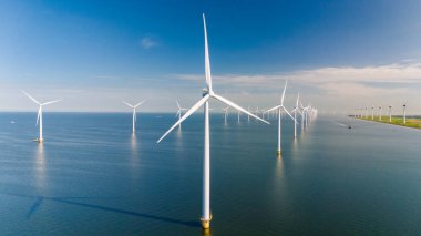 Yükselen rüzgar türbinleri zarif bir şekilde açık denizde dönüyor, rüzgarın gücünü kullanarak canlı bir gökyüzüne karşı temiz enerji üretiyorlar. Okyanustaki bir yel değirmeni parkının insansız hava aracı görüntüsü.
