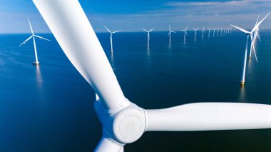 Geniş rüzgar türbinleri sakin denizin üzerinde zarifçe dönerek yenilenebilir enerjiyi yakalıyor ve Hollanda 'nın sürdürülebilirliğe olan bağlılığını gösteriyor. Okyanustaki bir yel değirmeni parkının insansız hava aracı görüntüsü.