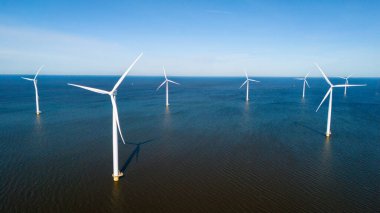 Dev rüzgar türbinleri sakin suların üzerinde zarifçe dönerek parlak mavi bir gökyüzünün altında yenilenebilir enerjiyi kullanırlar. Hollanda 'da bir yel değirmeni parkında insansız hava aracı görüntüsü