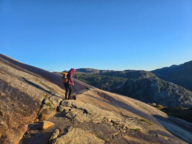 Yalnız bir yürüyüşçü engebeli bir arazide duruyor, Norveç 'in nefes kesen dağlarına ve vadilerine hayran, gün ışığında güneşleniyor. Lysefjord Kjeragbolten Kjerag Norveç