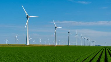 Tall wind turbines stand majestically against a vibrant sky, generating renewable energy amidst lush green fields in the Netherlands. clipart