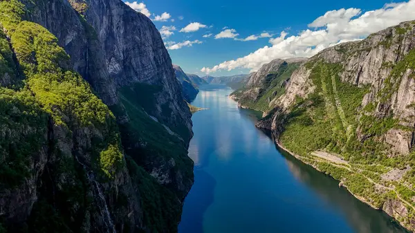 stock image Lush green cliffs rise steeply from tranquil waters reflecting a radiant sky, capturing the serenity of Norways breathtaking fjords. Lysefjord Lysebotn Norway