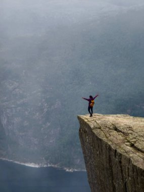 Kollarını uzatmış bir dağcı zaferle Preikestolen 'in kenarında duruyor, nefes kesen fiyortlarla ve sisli dağlarla çevrili..
