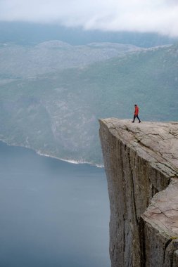 Canlı kırmızı ceketli yalnız bir yürüyüşçü sersemletici bir uçurumun kenarında duruyor. Sabah ışıklarıyla birlikte sisli Norveç fiyortlarına bakıyor. Önceki Norveç
