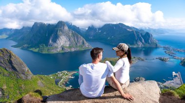 Bir çift, Lofoten Adaları 'nın görkemli dağları ve ışıldayan sularıyla çevrili göz kamaştırıcı manzarasına hayran bir şekilde bir kayanın üzerinde oturuyor. Reinebringen yürüyüşü Lofoten Norveç
