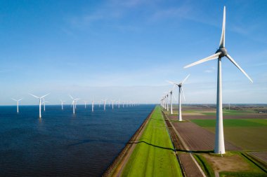 Uzun rüzgar türbinleri kıyı şeridi boyunca uzanır, geniş ve berrak bir gökyüzünün altında zümrüt çimenler ve mavi sularla uyum sağlarlar. Hollanda 'daki Ijsselmeer' de bir Alman hendeğinin yanında yel değirmeni türbinleri