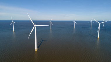 Uzun rüzgar türbinleri, Hollanda 'daki yenilenebilir enerjinin güzelliğini gösteren sakin suların üzerinde zarifçe dönerler. Yazın güneşli bir günde Hollanda 'daki yel değirmeni parkında insansız hava aracı görüntüsü
