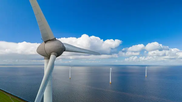 stock image Tall wind turbines rotate gently against a backdrop of serene waters and fluffy clouds, showcasing sustainable energy in harmony with nature. windmill turbines offshore and onshore in the Netherlands