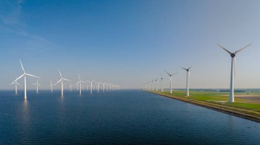 Rüzgar türbinleri Hollanda 'nın suları boyunca dimdik ayakta durarak berrak mavi gökyüzünün altında yenilenebilir enerjiyi kullanıyorlar. Westermeerdijk Ijsselmeer Hollanda Yel değirmeni Parkı