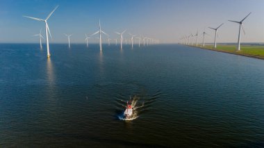 Ufuk boyunca uzanan yel değirmenlerinin çerçevelediği sakin sularda süzülen küçük bir balıkçı teknesiyle sakin bir akşam başlıyor. Hollanda 'da yel değirmenli balıkçı teknesi.