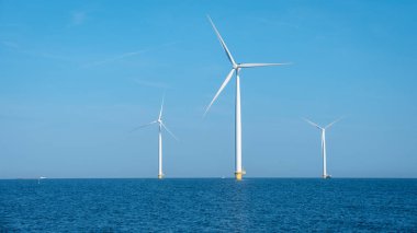 Heybetli rüzgar türbinleri ufukta dik durur, rüzgarın gücünü sakin ve yansıtıcı suların üzerinde kullanırlar. Kıyıdaki yel değirmeni parkı, Hollanda.