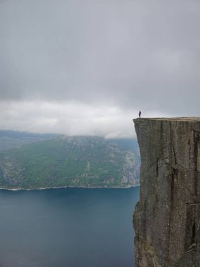 Cesur bir kaşif Preikestolen 'in kenarında duruyor, bulutlu bir gökyüzünün altında nefes kesici Lysefjord' a bakıyor..