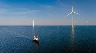 Hollanda 'da berrak bir gökyüzü altında görkemli yel değirmenleri tarafından çerçevelenen Ijsselmeer' in sakin sularında süzülen bir balıkçı teknesini, yel değirmeni parkı olan bir balıkçı teknesini huzurlu bir anda yakalıyor.