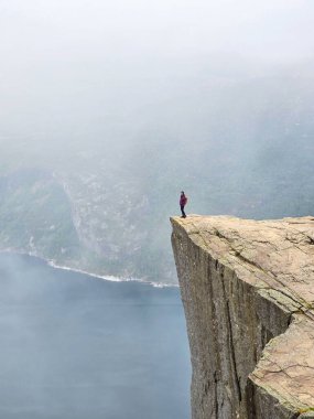 Yalnız bir figür dramatik bir uçurumun kenarında durur, aşağıdaki sisli ve dingin suyla çevrili, Norveç 'in vahşi doğasında macera ve yalnızlığın özünü yakalar. Önceki Norveç