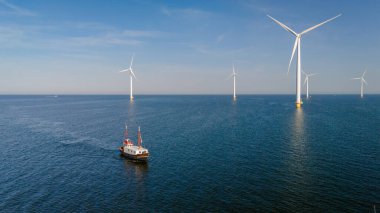 Hollanda 'daki berrak mavi gökyüzünün altında yüksek rüzgar türbinleriyle çevrili Ijsselmeer Gölü' nün sakin sularında bir balıkçı teknesi süzülüyor. Yel değirmeni parkı olan bir balıkçı teknesi.