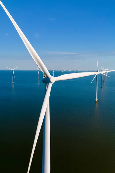 stock image Towering windmill turbines spin gracefully above shimmering waters, capturing the essence of green energy production in the serene Dutch landscape.