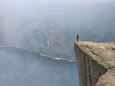 Yalnız bir yürüyüşçü, sis ve sakin fiyortlarla çevrili Preikestolen 'in kıyısından nefes kesici manzaralardan hoşlanır..