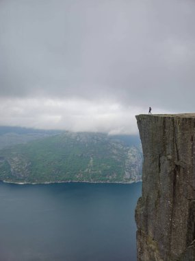 Yalnız bir yürüyüşçü dramatik Preikestolen uçurumunun kenarında duruyor, aşağıdaki Fiord 'un sakin sularına bakıyor..