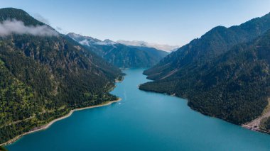 Plansee Gölü 'nün berrak suları etrafındaki dağları parlak mavi bir gökyüzünün altında yansıtıyor. Huzur ve keşfi davet ediyor. Plansee Avusturya