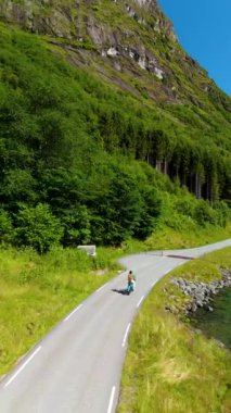 Bisikletli bir kadın, Norveç 'te güzel, dolambaçlı bir yol boyunca sakin ve huzurlu bir yolculuk yapıyor. Etrafı yemyeşil tepeler ve Lovatnet Gölü' ndeki görkemli dağlarla çevrili.