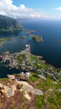 Reine köyünü ve Norveç 'in Lofoten adalarının çeşitli manzaralarını keşfedin. Reinebringen Loften dağının zirvesinde durup küçük adalara ve dağlara bakan bir çift adam.