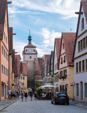 Rothenburg ob der Tauber, Almanya, 25 Ağustos 2024, Ziyaretçiler Rothenburg ob der Tauber 'in kaldırım taşı sokaklarında geziniyor, tarihi yarı ahşap binalara ve parlak mavi gökyüzü altındaki parlak renklere hayran kalıyorlar.