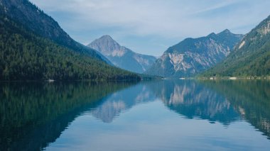 Buzlu sular Plansee Avusturya 'yı çevreleyen yüksek tepeleri yansıtıyor, güneşin doğuşunda doğanın çarpıcı yansımasını sergiliyor. Huzurlu atmosfer huzurlu bir tefekküre ve keşfe davet ediyor..