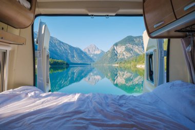 Awake to breathtaking views from a camper van nestled by the clear, tranquil waters of Plansee. The landscape features magnificent mountains mirrored in the lake, creating a peaceful atmosphere. clipart