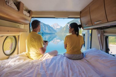 Bir çift, karavanda sakin bir sabahı kucaklıyor, Avusturya, Plansee 'deki dağların nefes kesici yansımalarına bakıyor, doğa ile çevrili huzurlu anların tadını çıkarıyor..