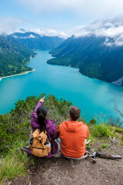 İki yürüyüşçü, verimli dağlar ve dingin sularla çevrili Avusturya 'daki Plansee' nin çarpıcı manzarasını takdir etmek için ara verdi. Doğa güzelliği, bu sükunet anını paylaştıkça gözler önüne seriliyor..