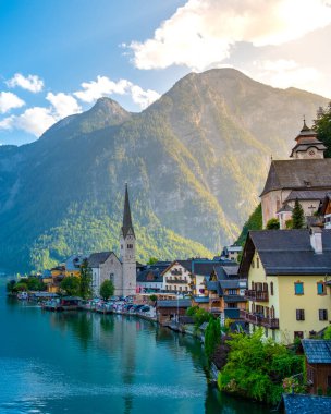 Avusturya 'nın Hallstatt kentinin pitoresk köyünde, dingin evler gölün sakin kıyıları boyunca uzanır, muhteşem dağlar parlak bir gökyüzünün altında dramatik bir şekilde yükselir..