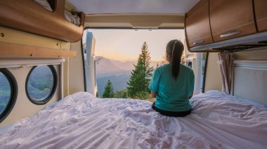 Sıcak bir karavana yerleşmiş bir insan, güneş ışığının pencereden akarak Avusturya 'nın Hallstatt kentinin nefes kesen manzarasına sıcak bir parıltı saçarak huzurlu bir sabahın tadını çıkarıyor..