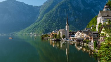 Avusturya 'nın Hallstatt kentinde sakin bir sabah, durgun suya yansıyan büyüleyici göl kenarındaki evlerin arka planında görkemli dağların manzarası yer alıyor..