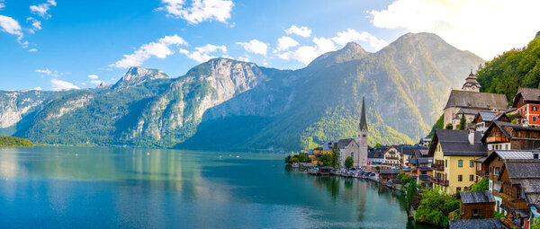 Nestled between majestic mountains, the picturesque village of Hallstatt awakens under the golden rays of sunrise, casting vibrant reflections on the serene lake, inviting exploration and tranquility.