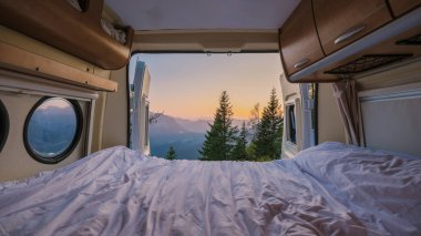 Bir karavanın içinde, güneş doğarken sıcak yatak örtüsü dışarıdaki nefes kesen dağları rahatlatıyor. Yemyeşil ağaçlar manzarayı çerçeveler, sakin Avusturya manzarasında maceraya davetiye çıkarır.