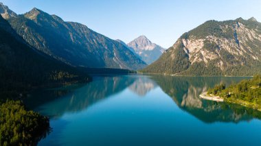 Huzurlu bir göl etrafındaki yüksek dağları yansıtarak Avusturya, Plansee 'de manzaralı bir alp manzarası yaratır. Berrak mavi sular doğal güzelliği yansıtıyor, sükuneti davet ediyor..