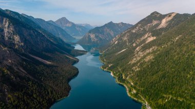Plansee 'nin çarpıcı turkuaz sularının üzerinde görkemli dağlar yemyeşil sularla çevrili olarak dik bir şekilde yükselir. Huzurlu göl gökyüzünü yansıtıyor, sakin bir manzara yaratıyor doğa severler için mükemmel..